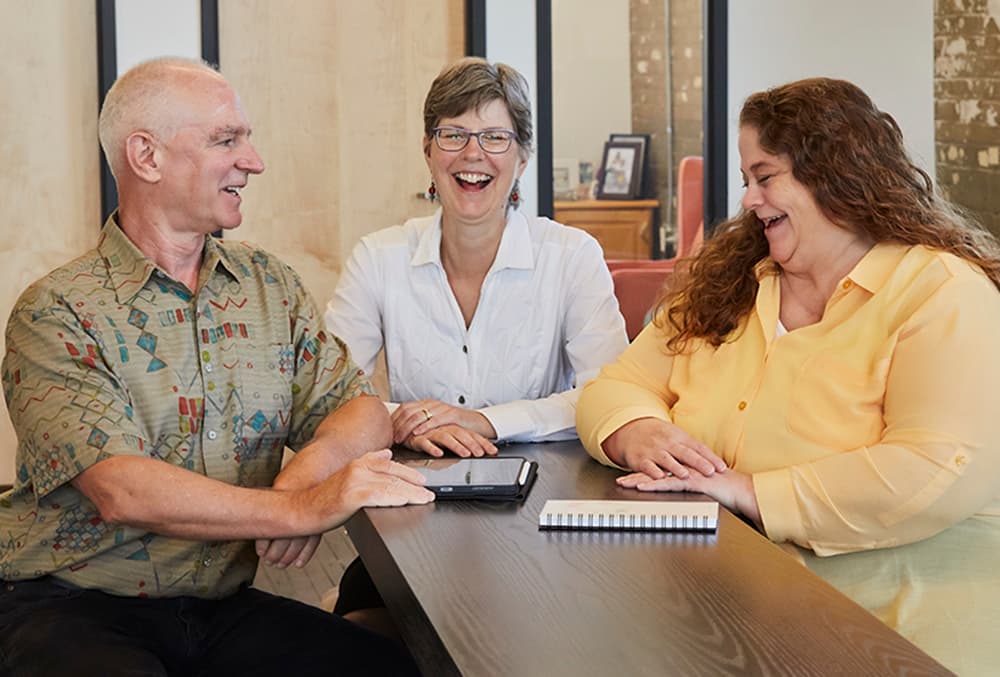 Dave Lasecke, Joyce Lasecke, and Robin Lucas laughing together around a table.