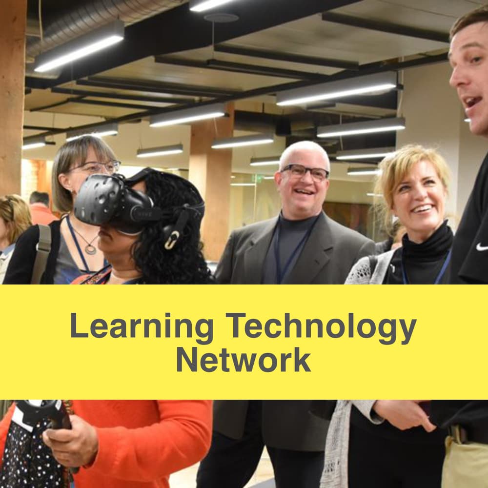 Learning technology network caption, image of community members chatting near one woman using a virtual reality headset